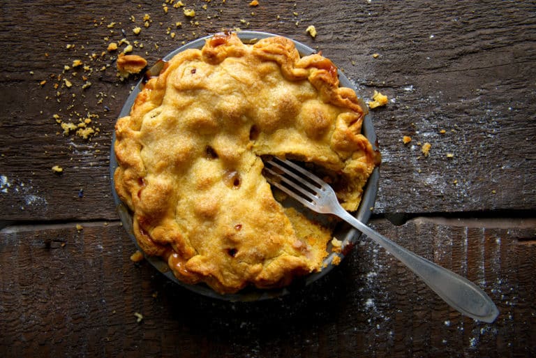 A delicious warm, baked apple pie with one slice removed and a fork placed in the centre